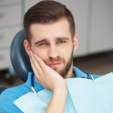 Man in dental chair holding jaw in pain