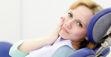 Woman in dental chair holding jaw in pain